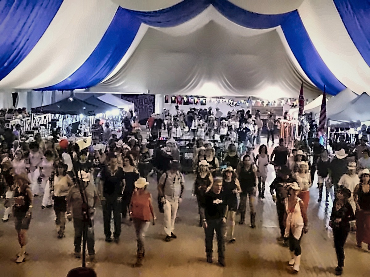 Públic ballant line dance en línia sobre la pista de la carpa del festival
